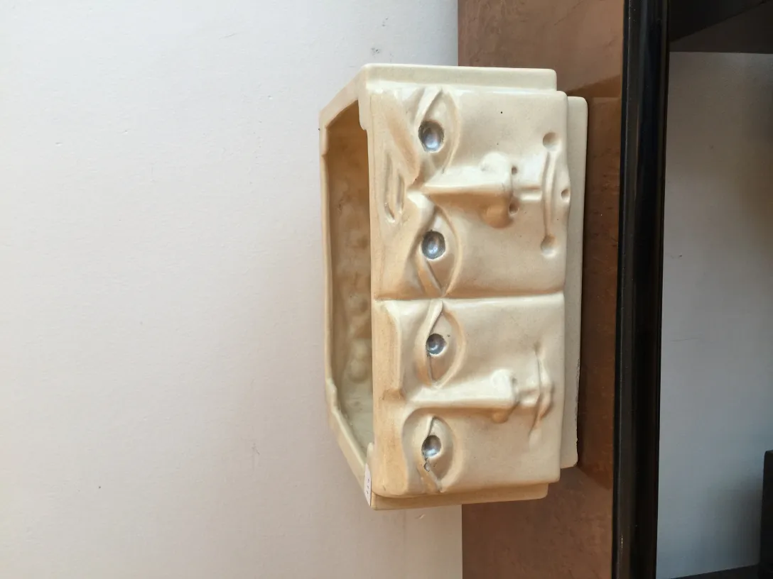 Escultura de cerâmica antiga com rostos em relevo, fundo branco.