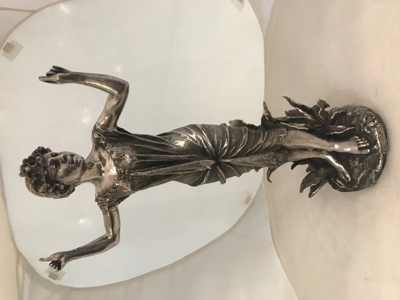 Escultura antiga de figura masculina em pose expressiva, com elementos naturais na base.