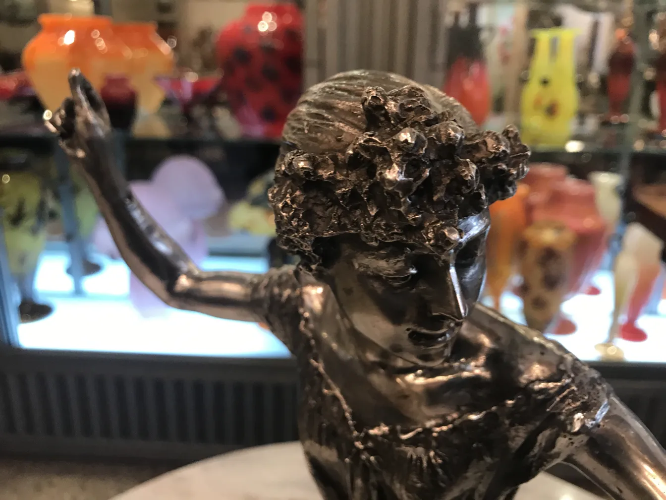 Sculpture ancienne d'une femme avec des cheveux ornés de fleurs, entourée de vases colorés.