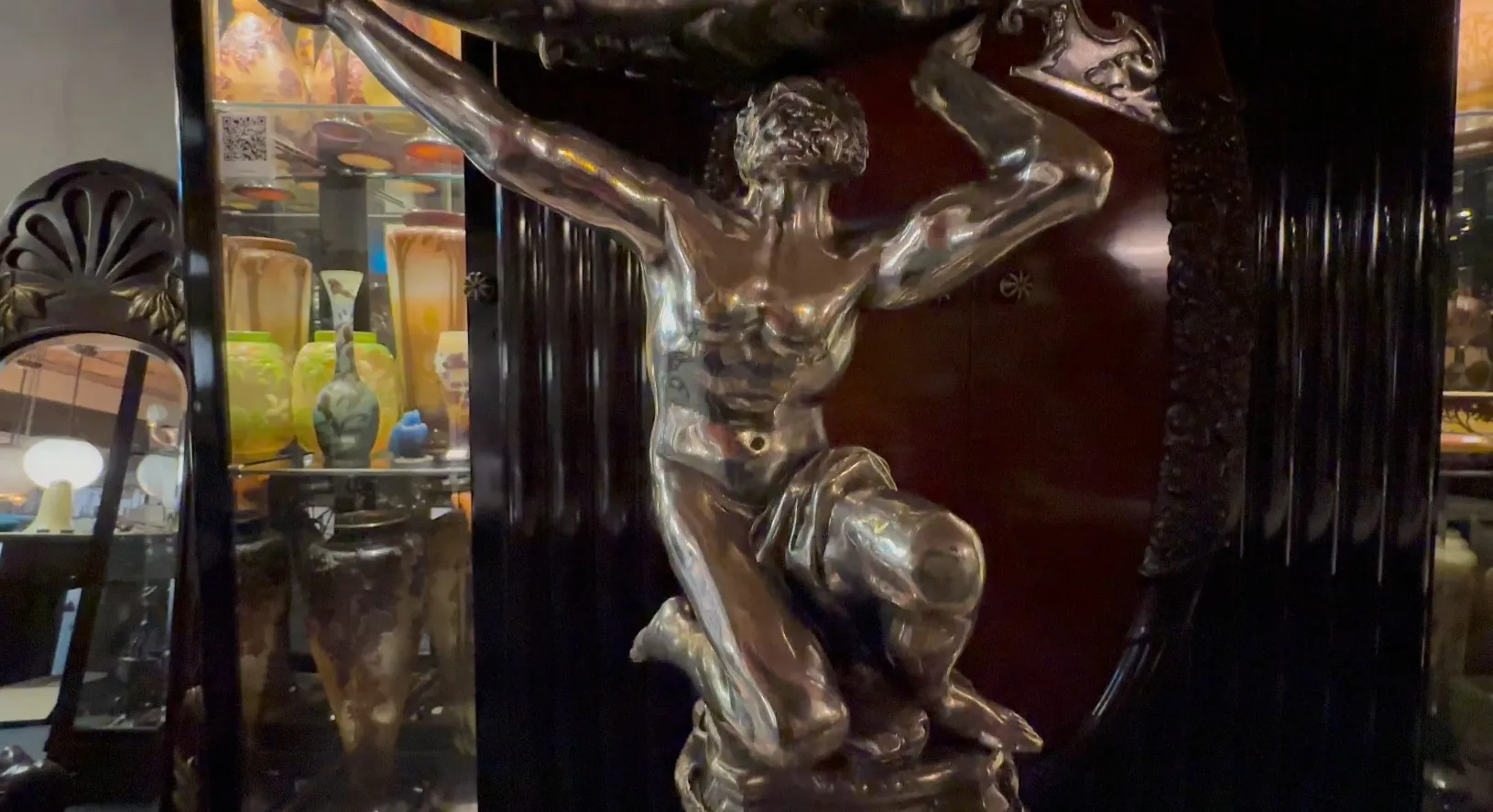 Antique sculpture of a human figure holding an object, varied background of antiques.