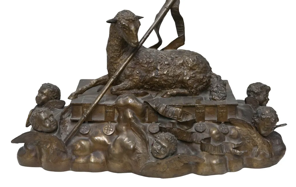 Escultura antiga de um cordeiro sobre um livro, cercada de anjos.