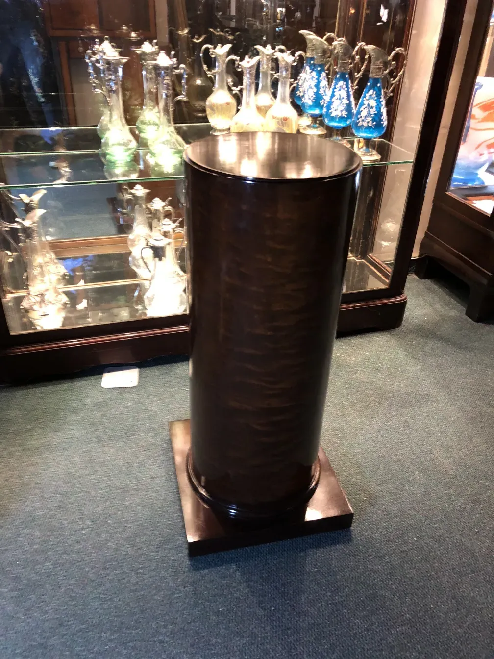 Antike dekorative Säule mit glänzender Oberfläche und solider Basis, umgeben von Kristallfiguren.