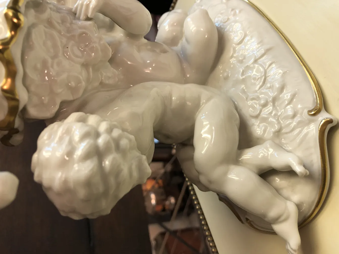 Figura antiga em cerâmica branca de uma criança com detalhes dourados, ambiente encantador.