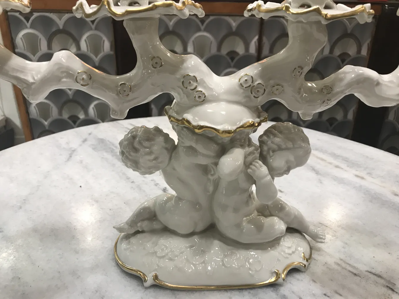 Candelabro antico in ceramica bianca con dettagli dorati e figure infantili