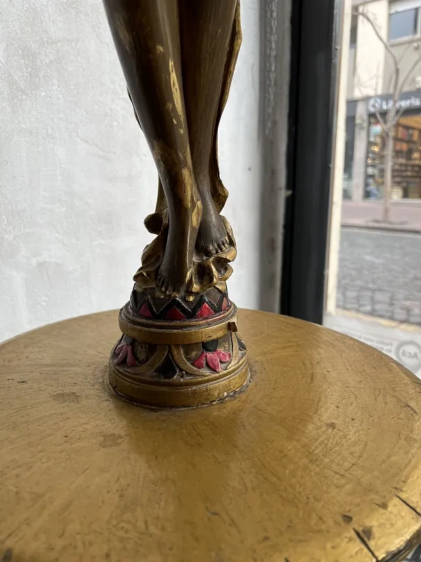 Escultura antiga com base dourada e detalhes vermelhos e pretos, destacando pés.