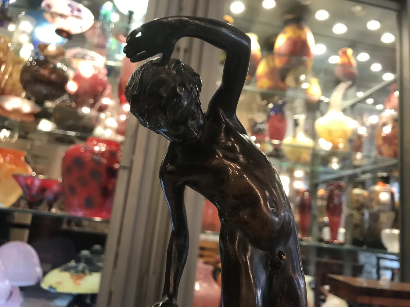 escultura antiga de um homem com um gesto dinâmico, cercada por antiguidades coloridas.