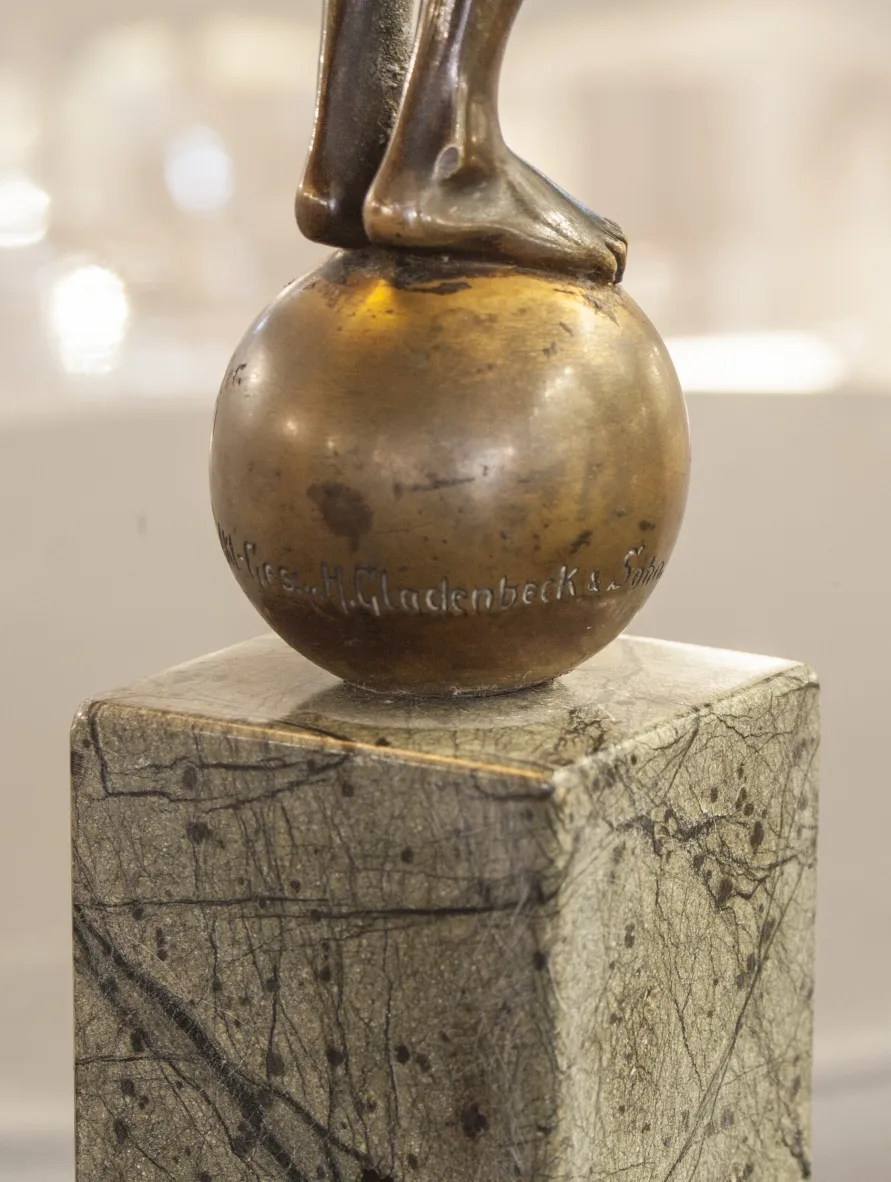 escultura antigua con figura sobre bola en base decorativa