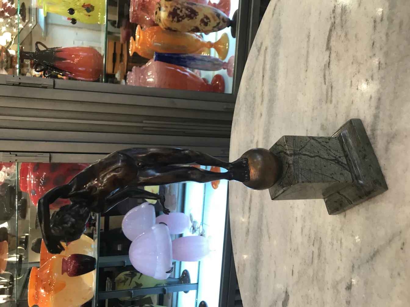 antique sculpture depicting a slender human figure, glass decorations in the background