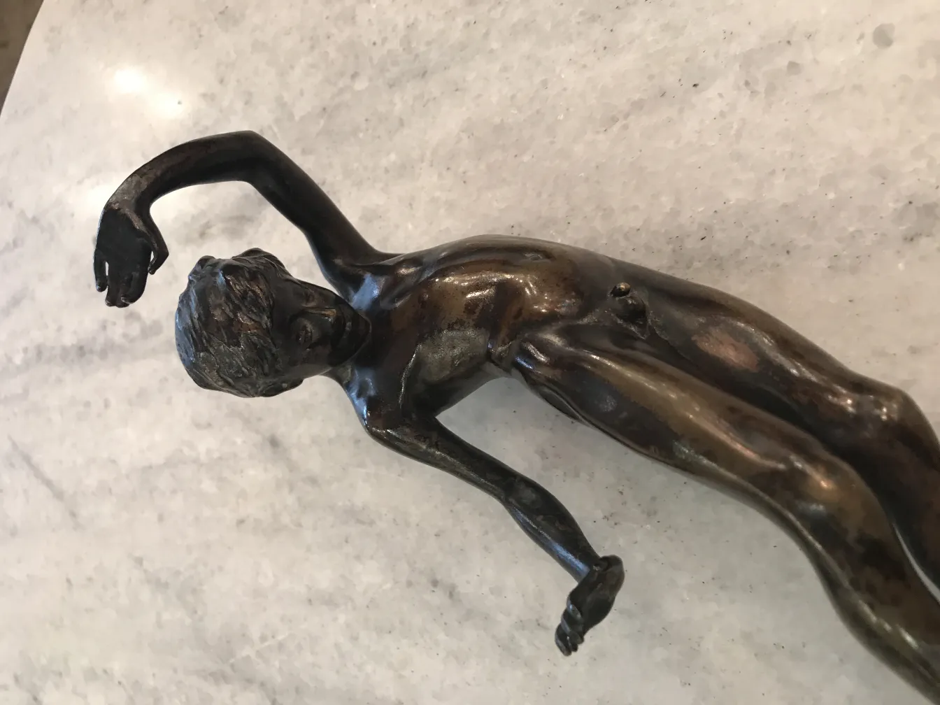 Scultura antica di figura umana con dettagli fini, sfondo chiaro.