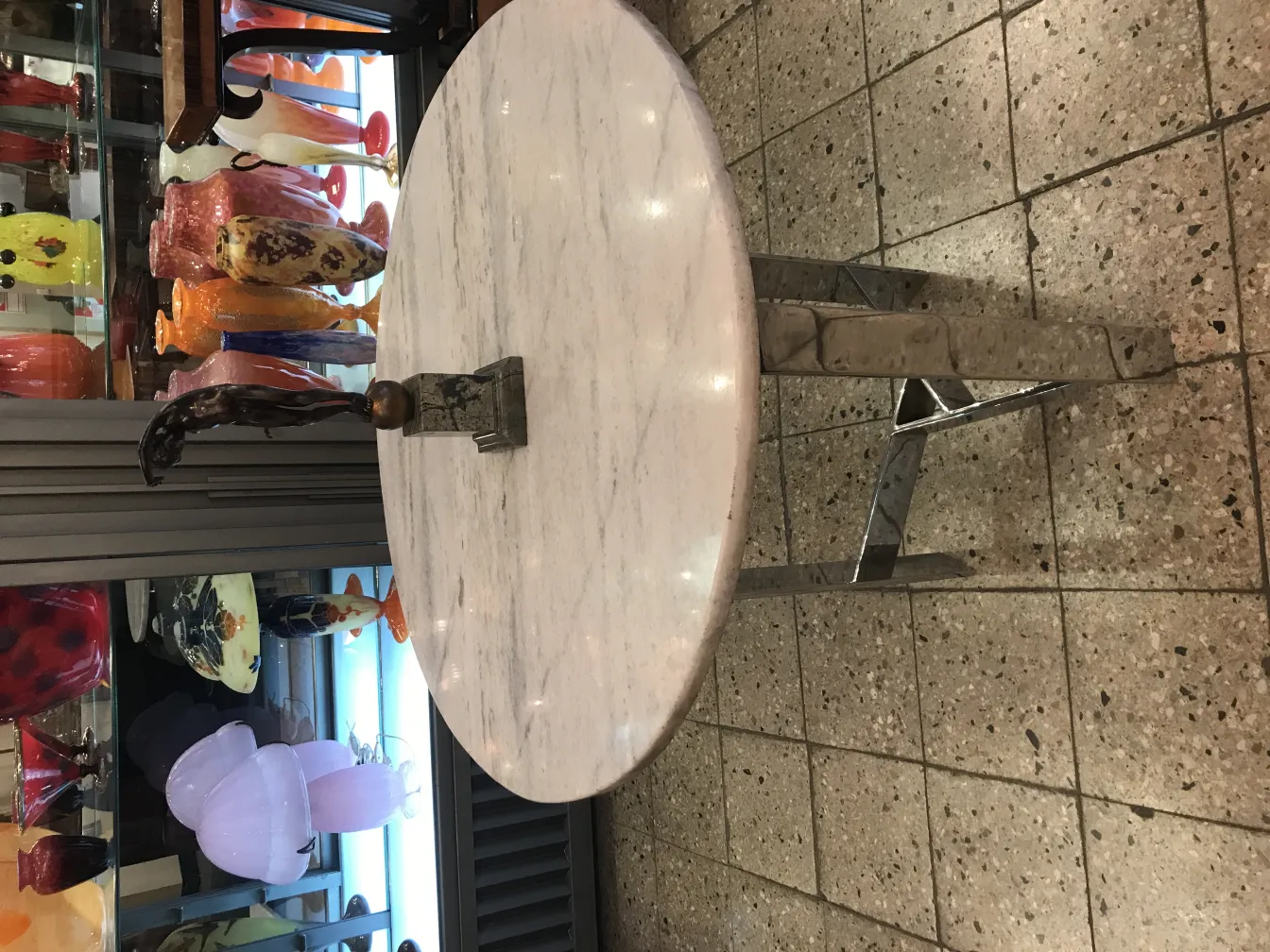 Escultura antigua decorativa con forma estilizada y base metálica, en un entorno de vitrinas brillantes.