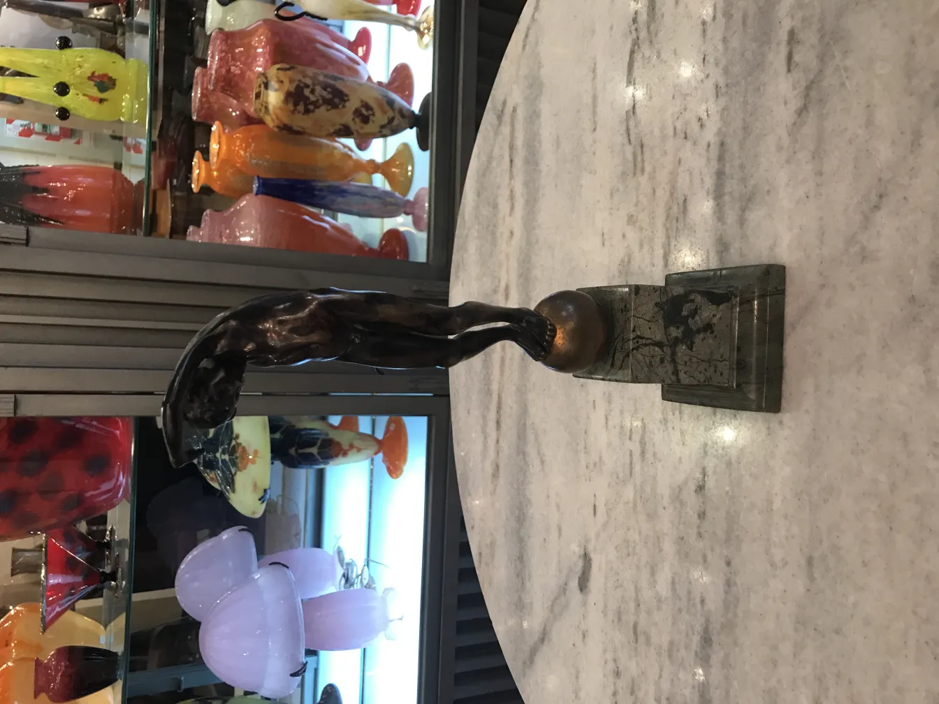 Escultura antigua de figura con base presenta detalles únicos y forma estilizada, rodeada de objetos decorativos.