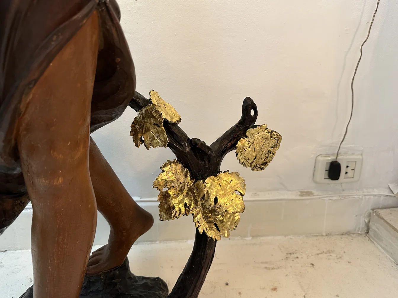 Scultura antica di figura umana con foglie d'oro alla base.