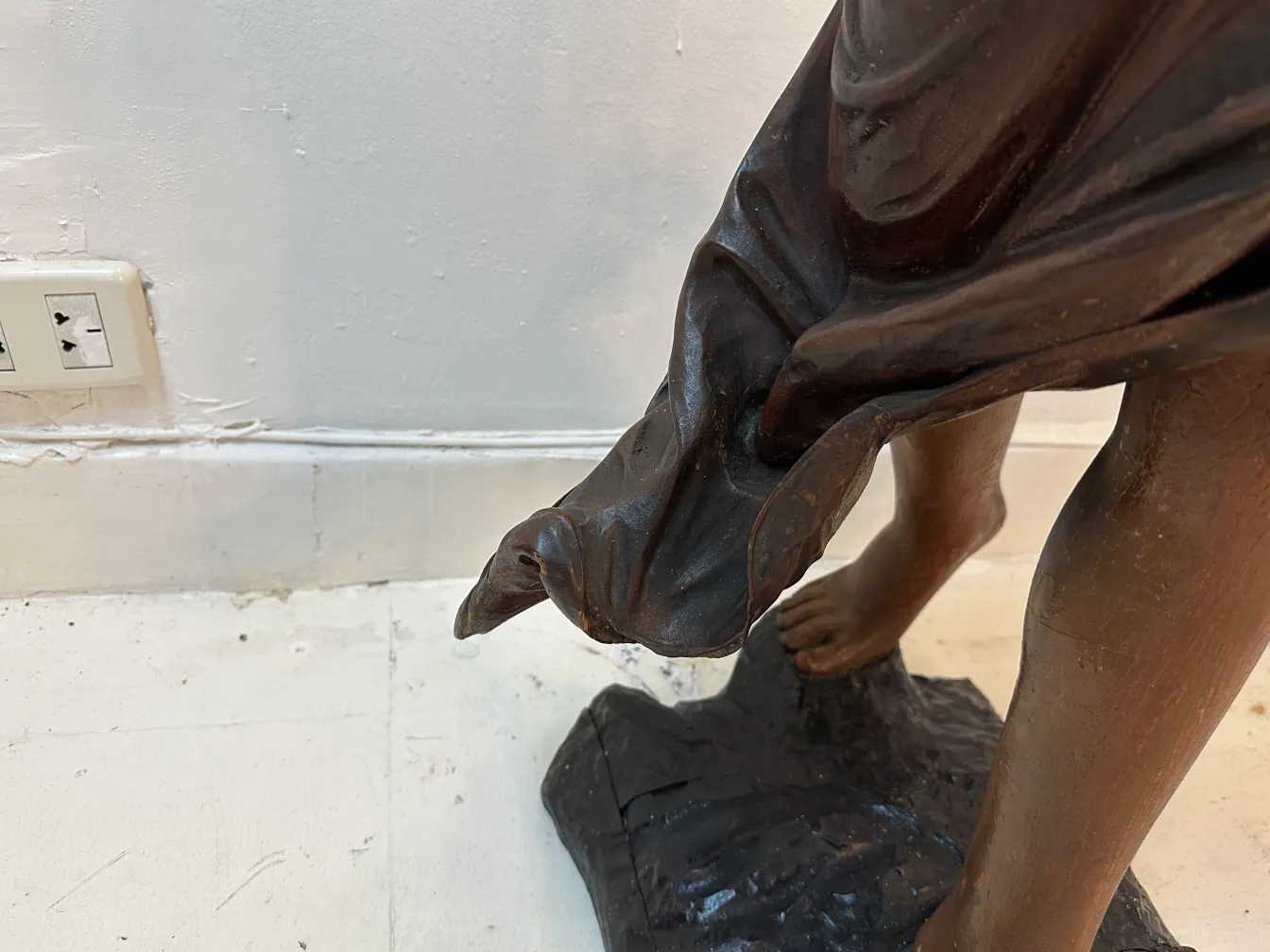 Detail einer antiken Skulptur, die einen Fuß und drapierten Stoff zeigt.