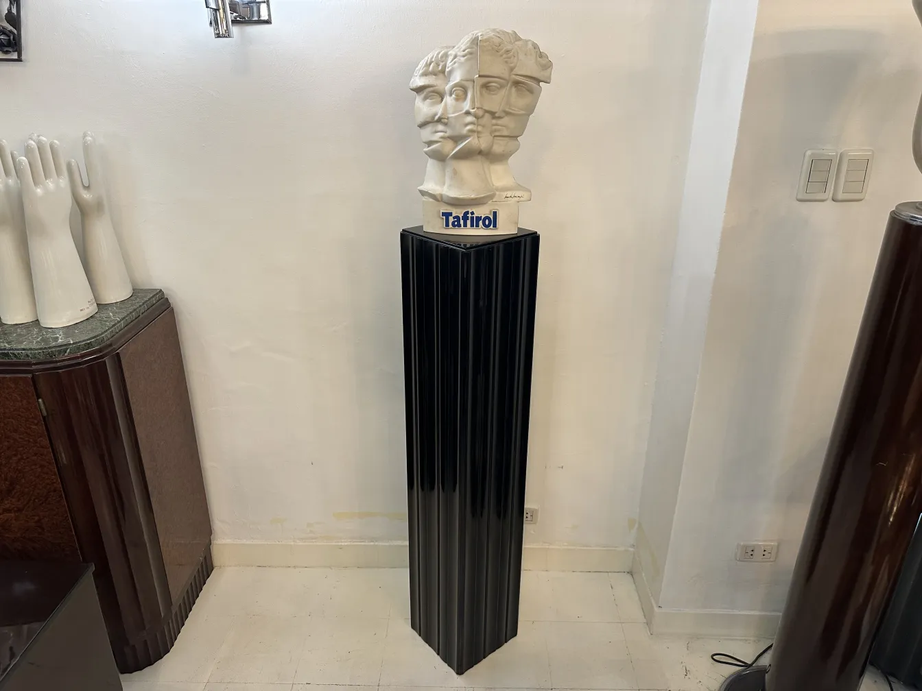 Coluna antiga preta com uma escultura em cima. Ambiente moderno.