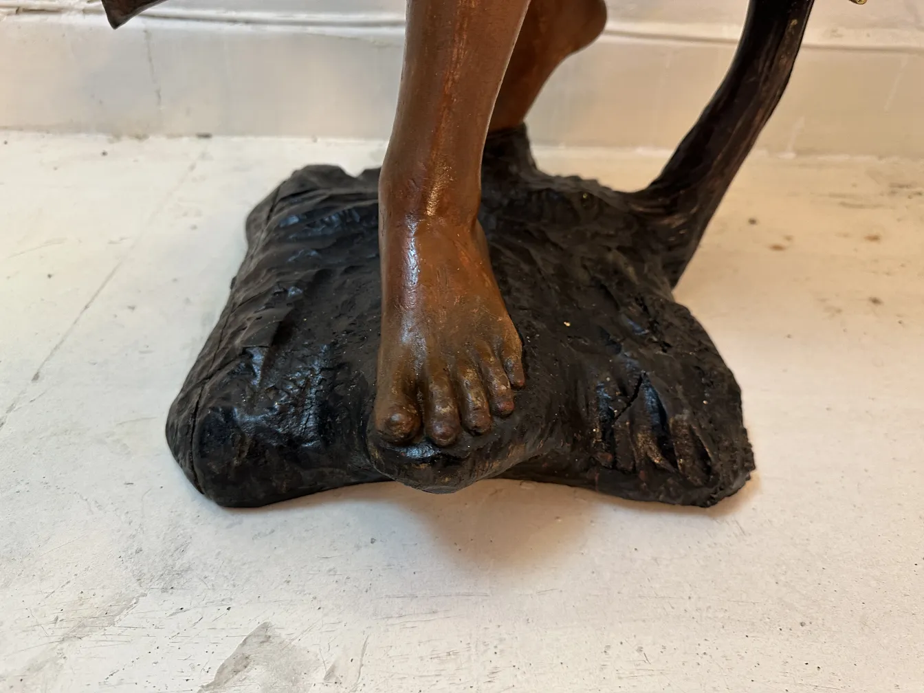 Antique sculpture featuring a foot resting on a textured base, neutral setting.
