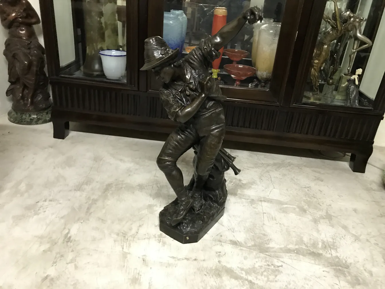 escultura antigua que muestra a un hombre en acción, con fondo variado de antigüedades