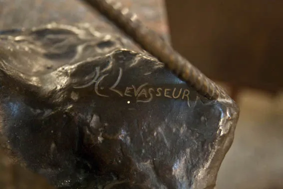 Escultura antiga com assinatura visível e detalhe sutil.