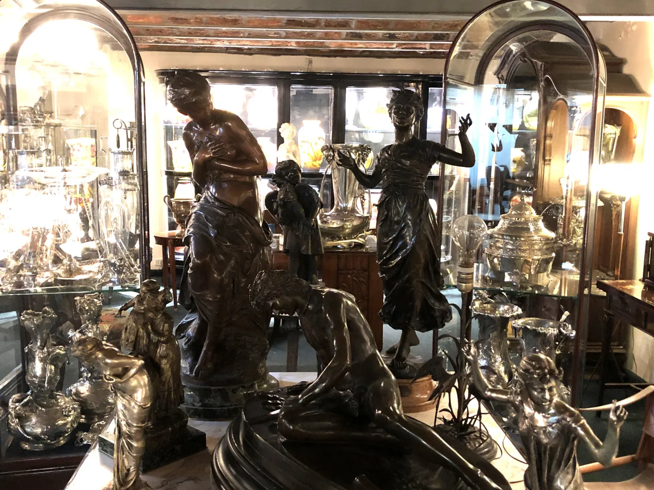 Sculpture figurative antique dans une vitrine, entourée d'objets décoratifs anciens.