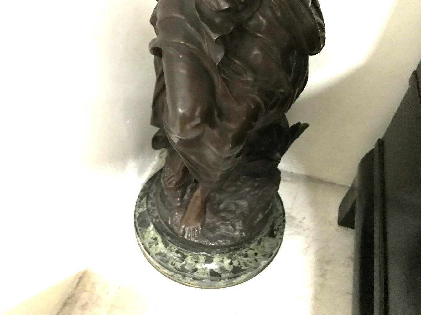 scultura antica di un personaggio con dettagli decorativi e base verde