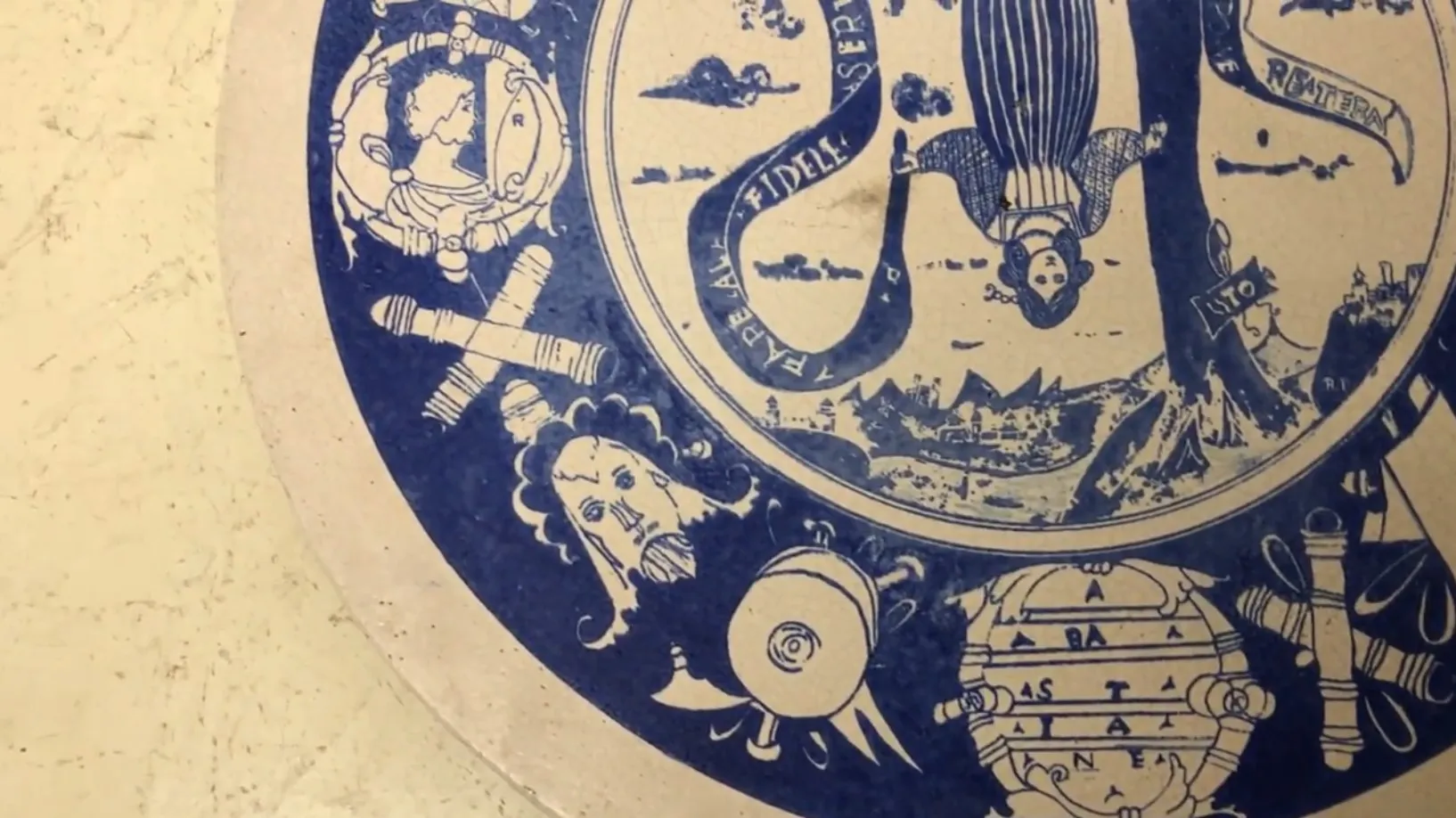 Assiette en céramique antique avec un design bleu détaillé, montrant des figures et des paysages.