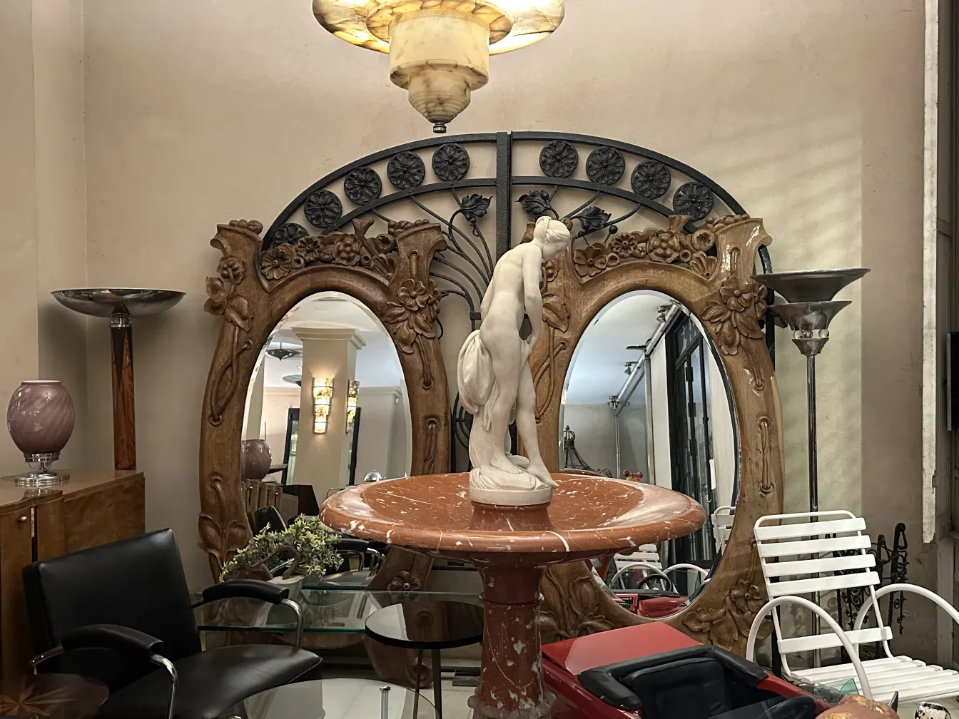 Escultura antiga em mármore branco em um espaço decorativo com espelhos, móveis e lâmpadas.