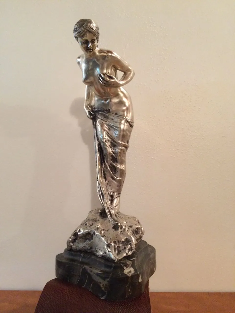 Scultura di donna antica con finitura lucida che tiene un drappeggio.