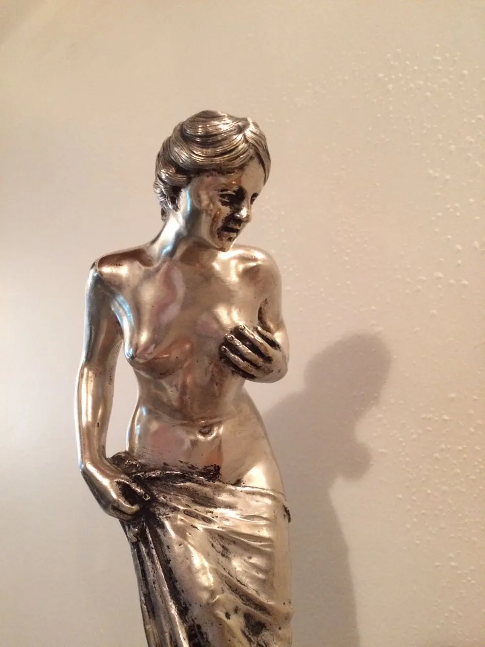 Antike Metalldarstellung einer menschlichen Figur mit realistischen Details. Schlichte Umgebung.