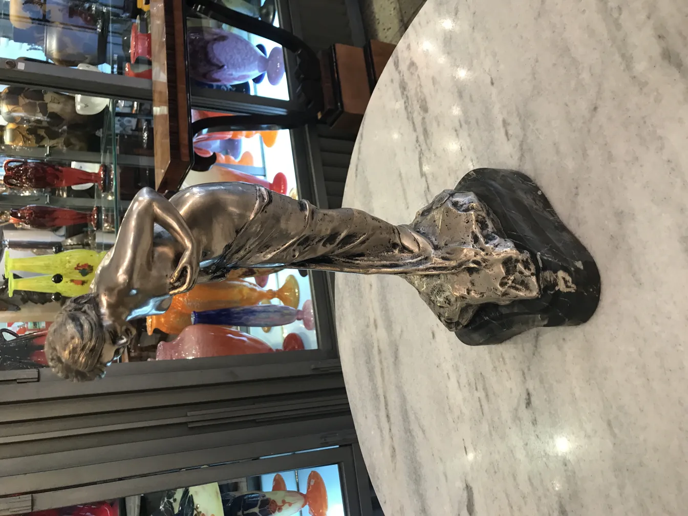 Escultura antigua de figura elegante con base oscura, en ambiente variado.