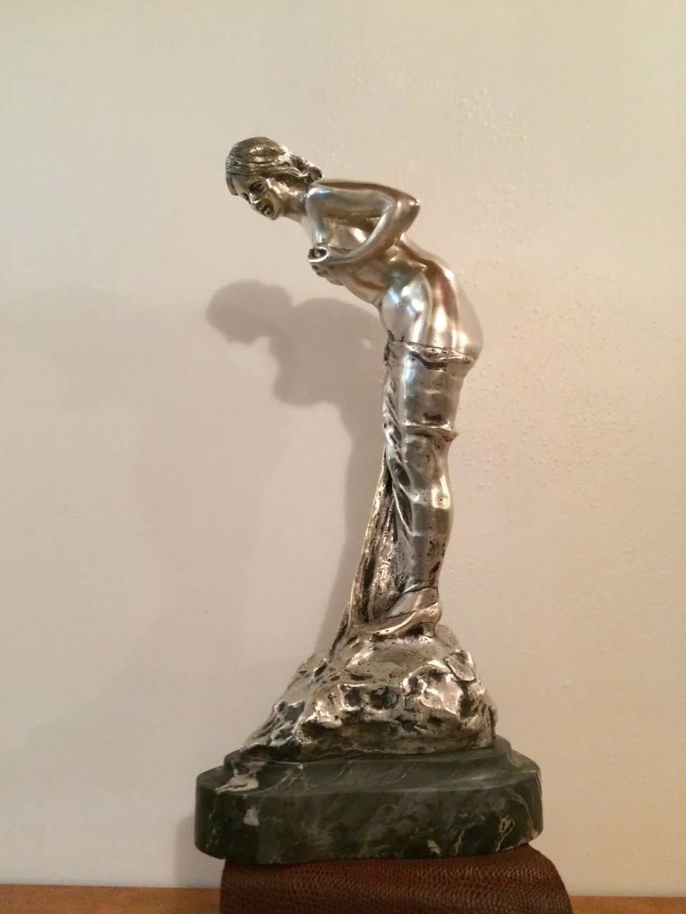 Escultura antiga de figura feminina com detalhes elegantes em fundo neutro