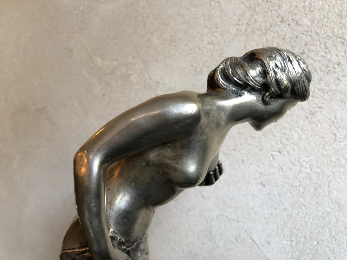 Escultura antiga de figura feminina em pose inclinada, detalhes realistas.