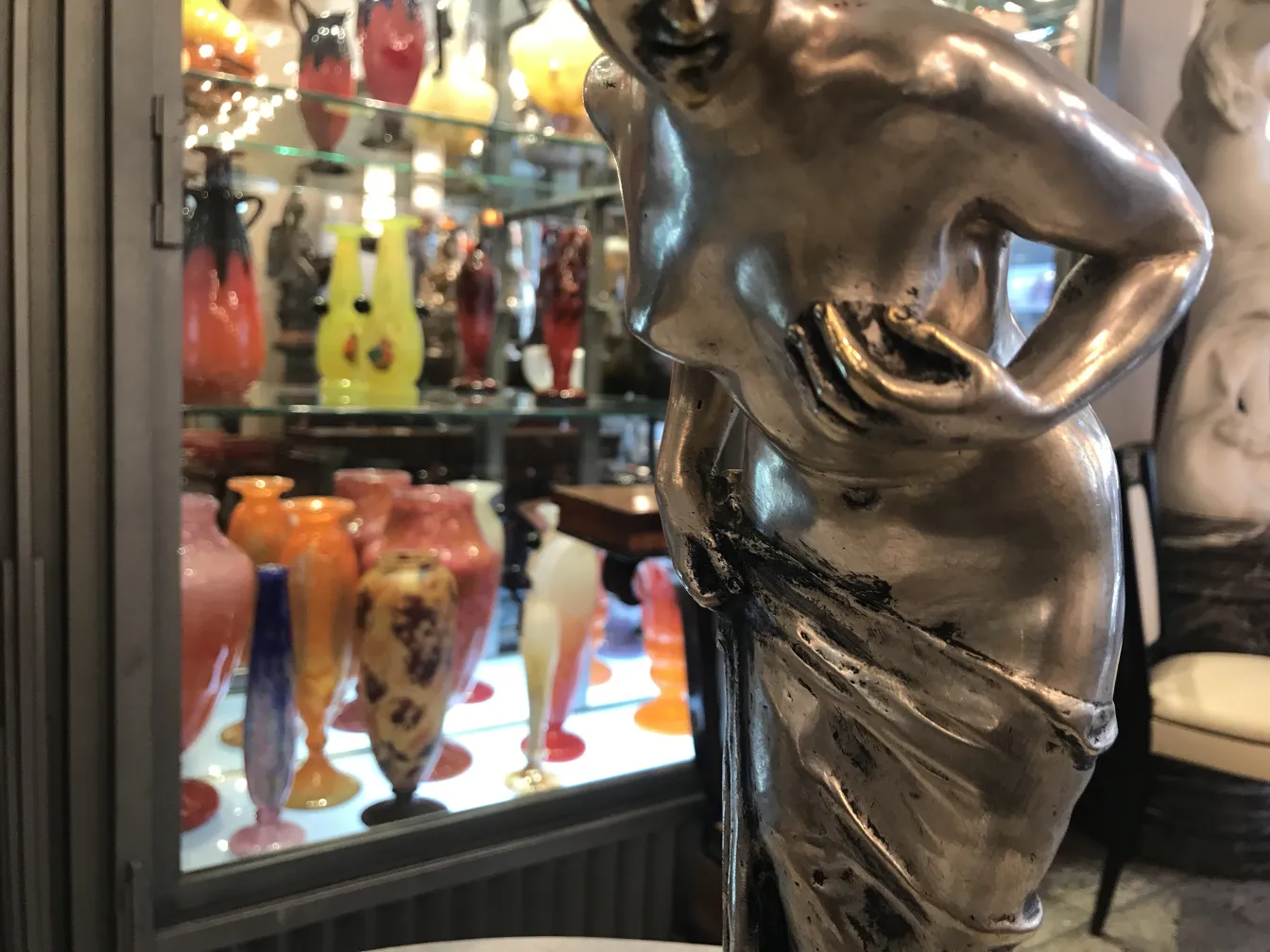 Antica scultura di figura femminile con vasi colorati sullo sfondo.
