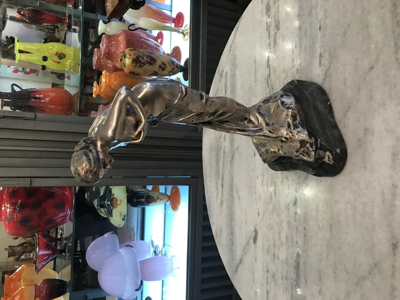 Antike Skulptur einer Frau aus Bronze, detailliert und elegant vor einem Hintergrund dekorativer Gegenstände.