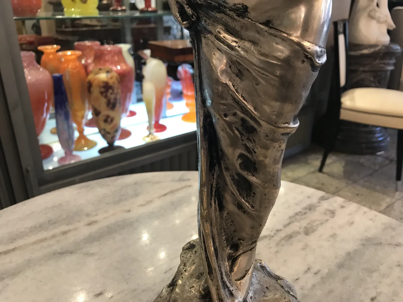 Dettaglio di una scultura antica con drappeggio, circondata da oggetti in vetro colorati.