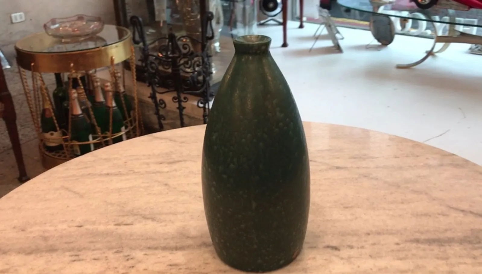 Vaso antiguo de cerámica verde en una mesa de mármol, rodeado de antigüedades.