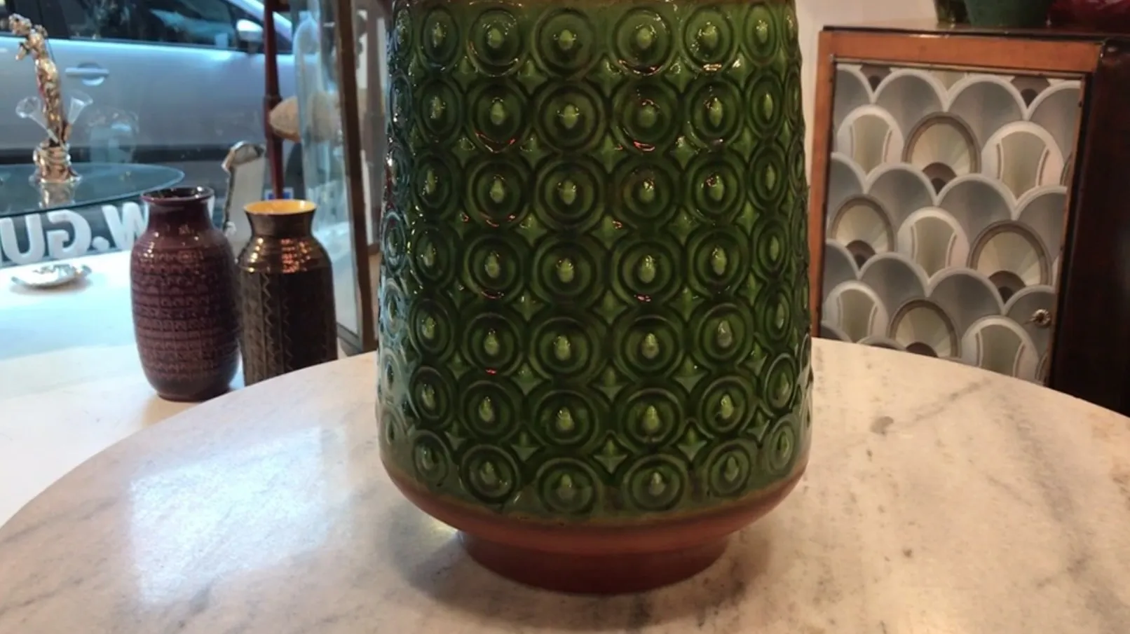 Vase en céramique ancienne de couleur verte avec des motifs circulaires sur un fond ivoire.