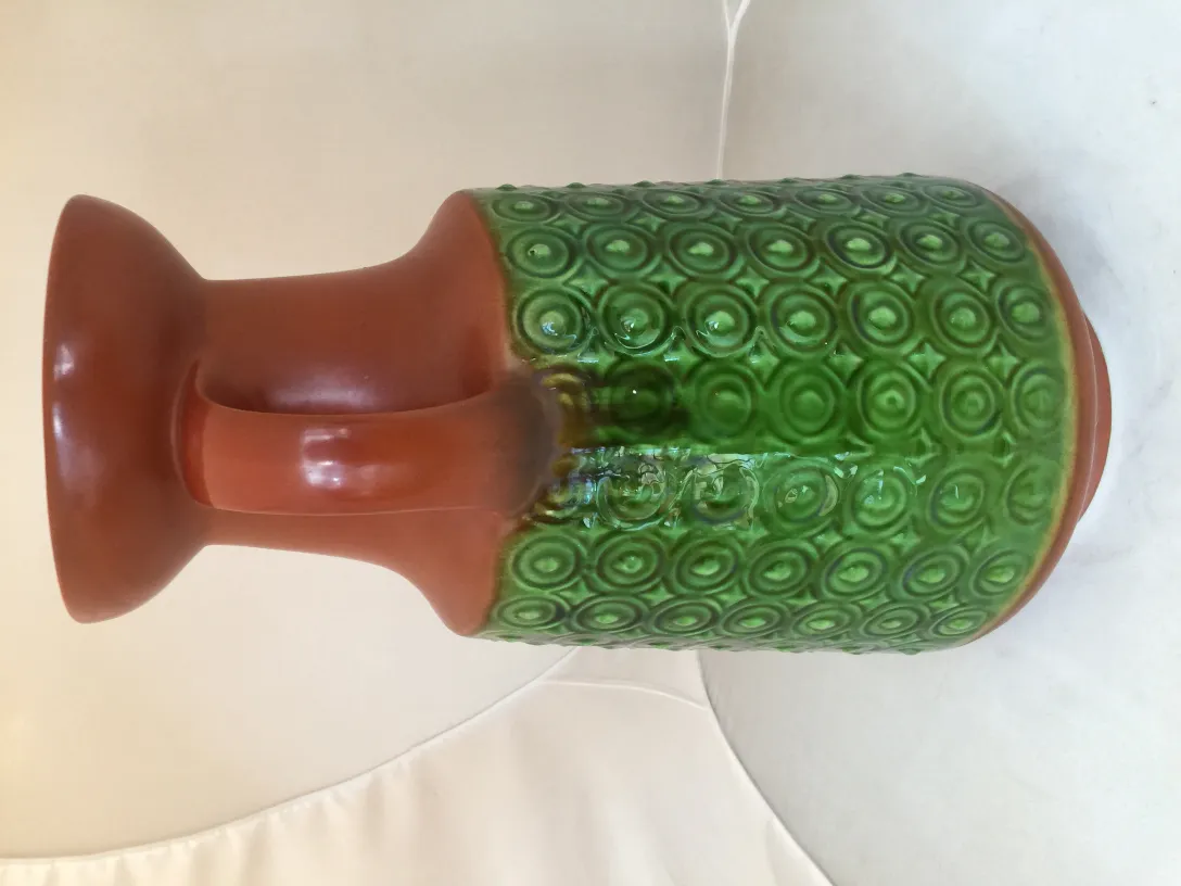 Vaso antico in ceramica con design verde e marrone, su uno sfondo chiaro.