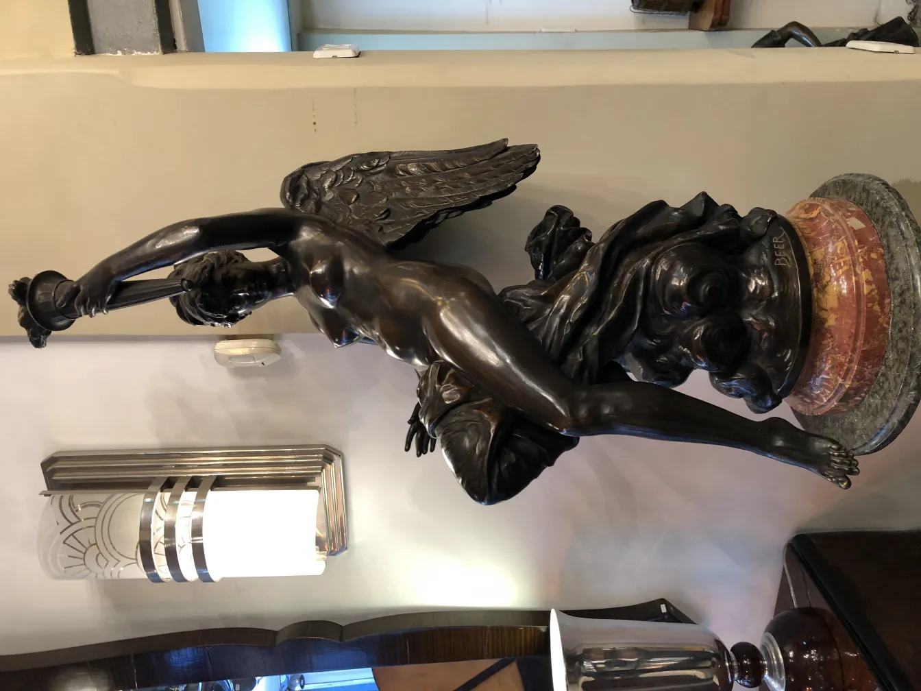 Sculpture antique d'une figure féminine ailée avec une base décorative dans un cadre élégant.