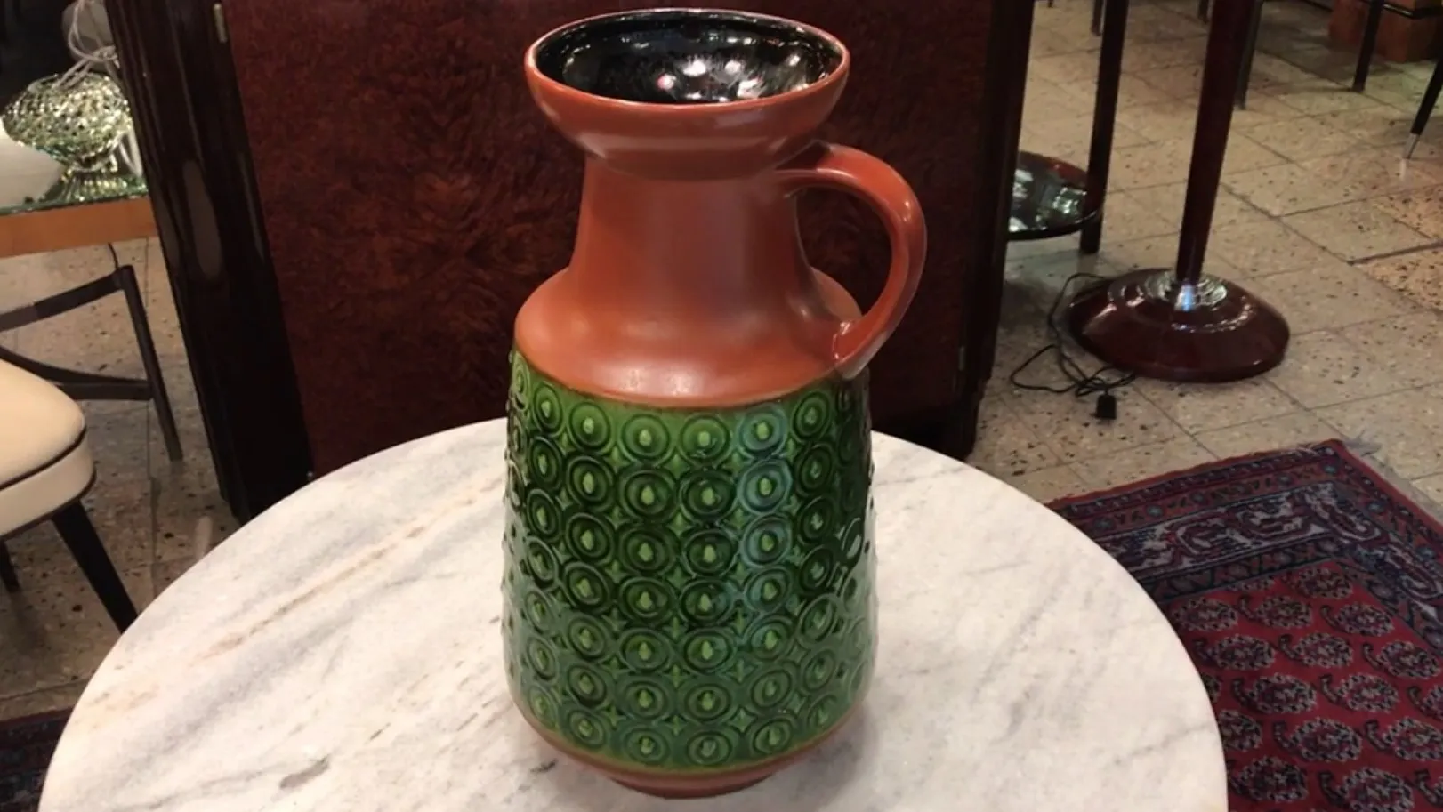 Antiker grüner Keramikkrug mit dekorativem Design auf einem Marmortisch.