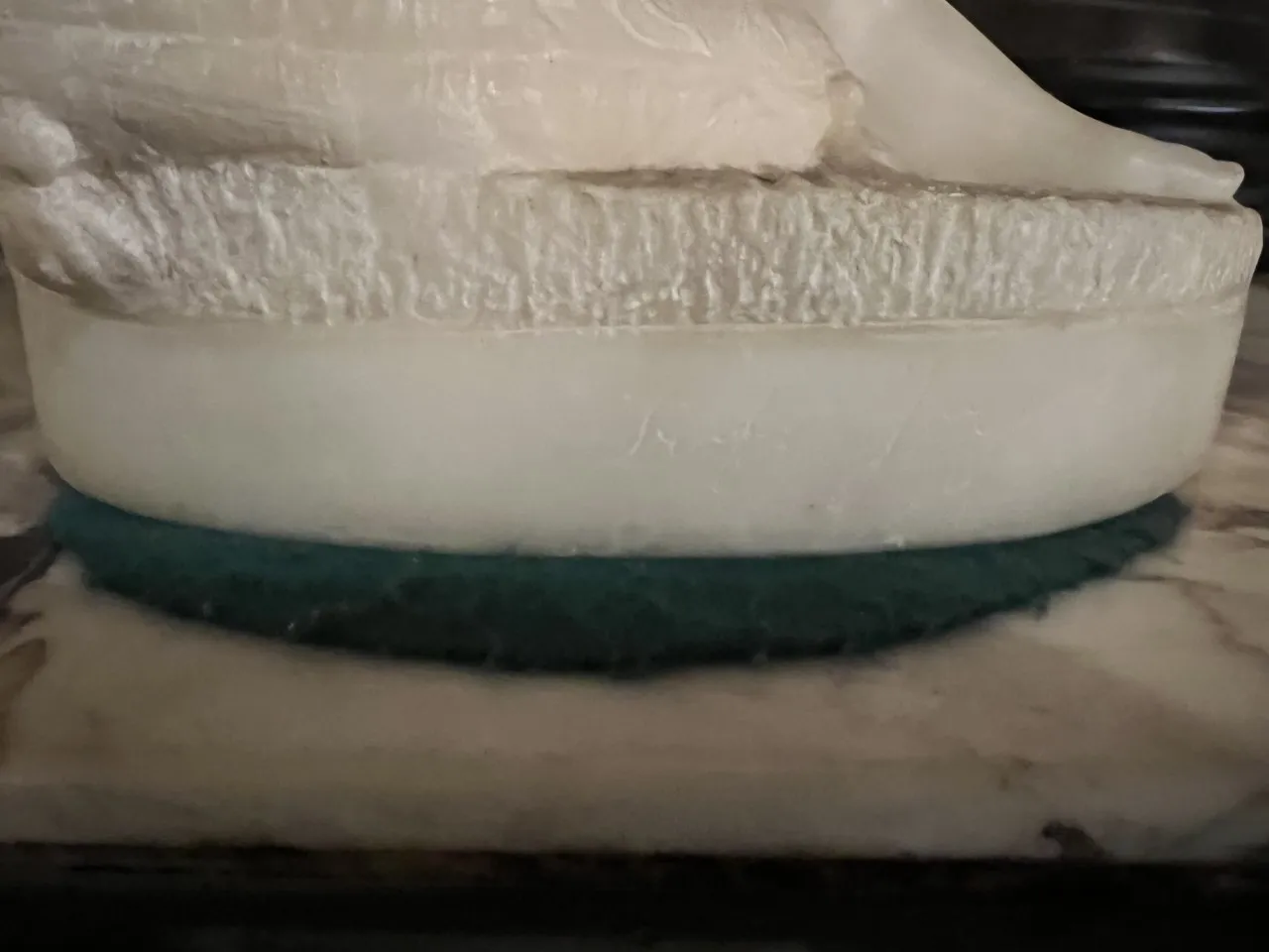 Dettaglio di scultura antica con base in marmo e tessuto verde.