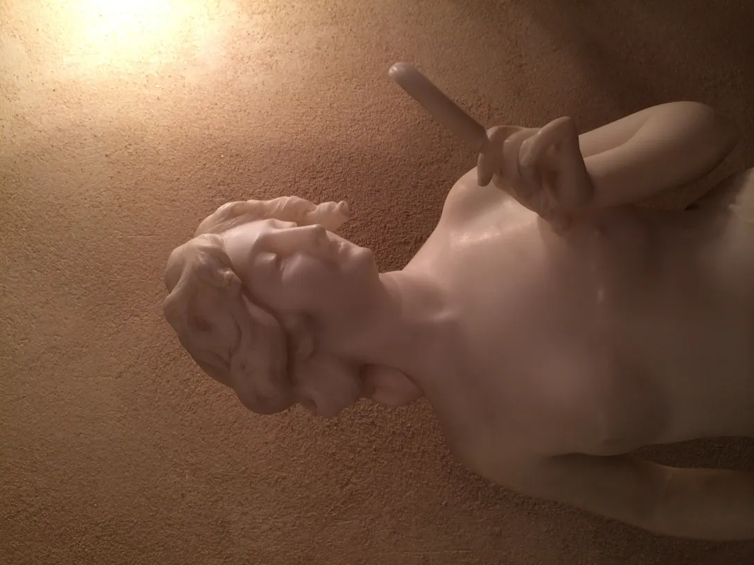 Scultura antica di donna che fa un gesto, con uno sfondo sottile.