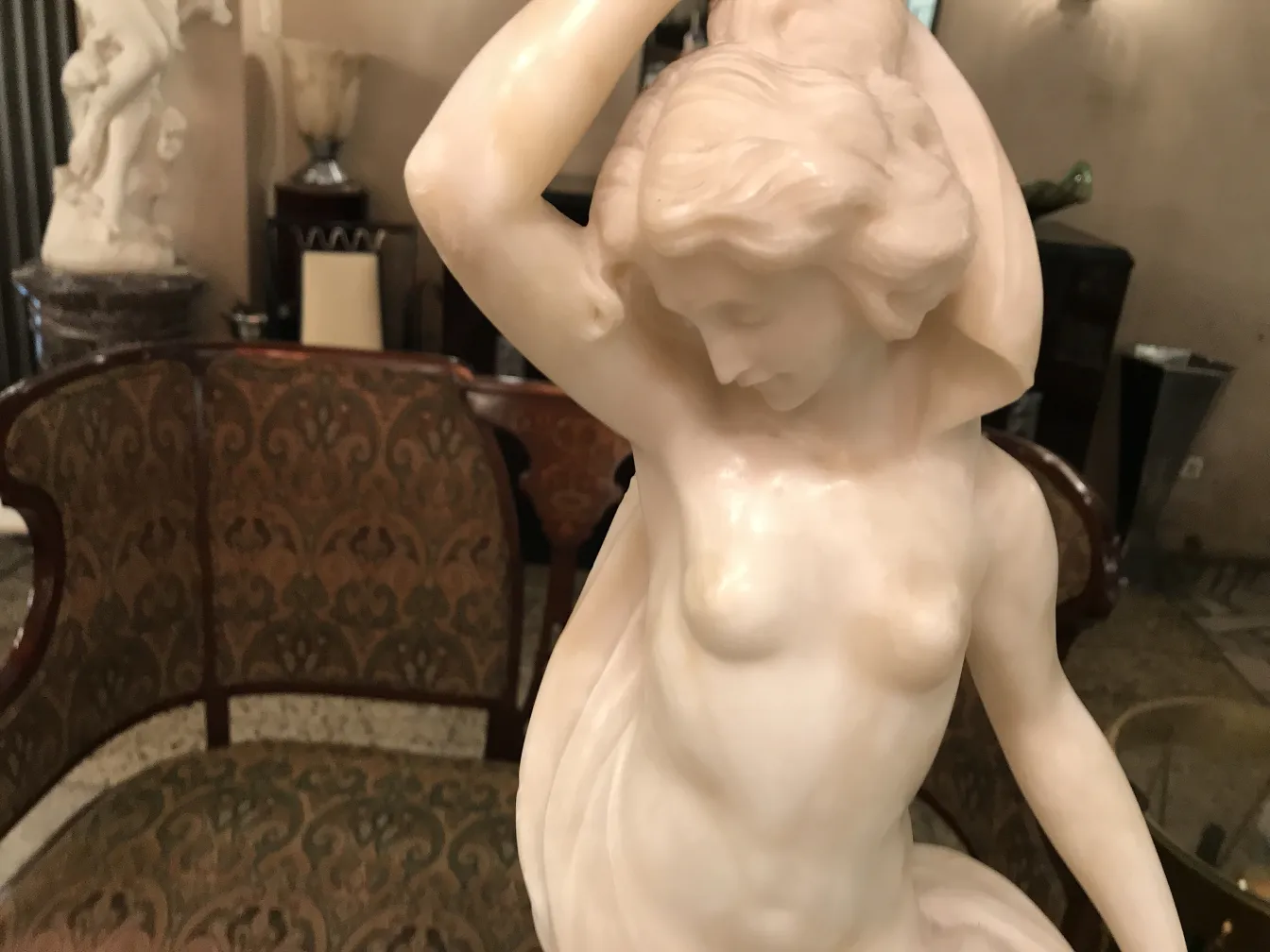 Escultura antigua de una mujer en pose elegante, fondo decorativo.