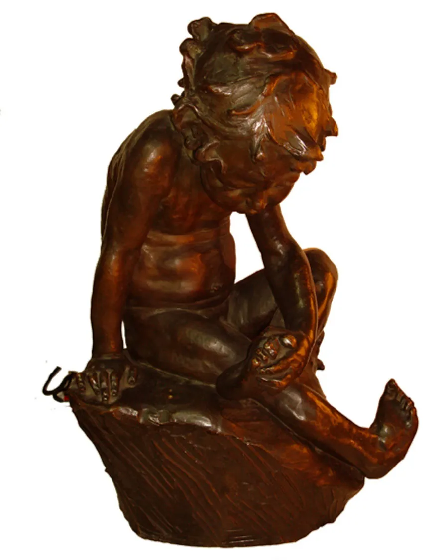 Scultura antica di un bambino seduto, che mostra concentrazione, in un ambiente sobrio.