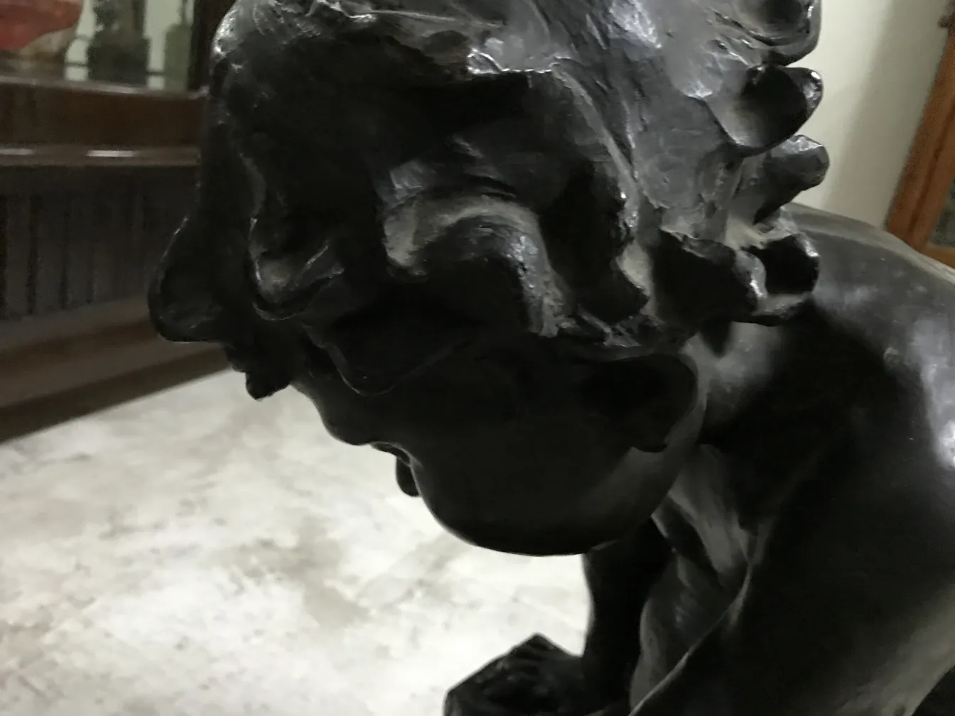 प्राचीन मूर्ति का विवरण, गहरे रंग का और अभिव्यक्ति में संवेदनशीलता, एक पारंपरिक परिवेश में।