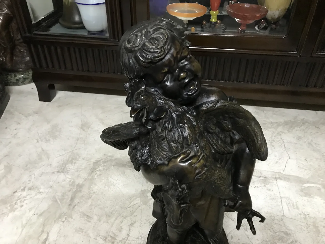 sculpture ancienne d'un enfant étreignant un coq dans un cadre classique