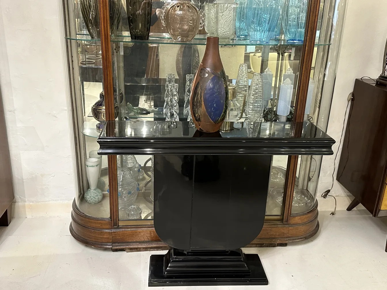 Jarrón de cerámica antigua con formas estilizadas, rodeado de objetos decorativos claros en un entorno elegante.