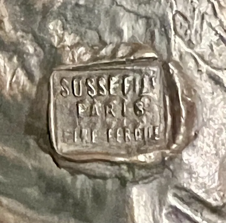 Antigua escultura con firma de Jane Le Soudier en primer plano.