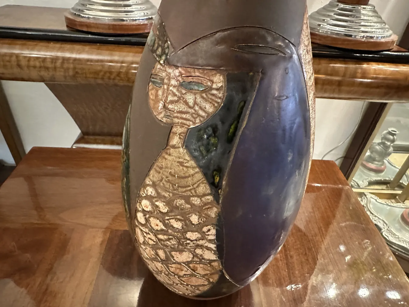 Vaso de cerâmica antiga com decorações intrincadas, figura feminina em tons escuros e dourados.
