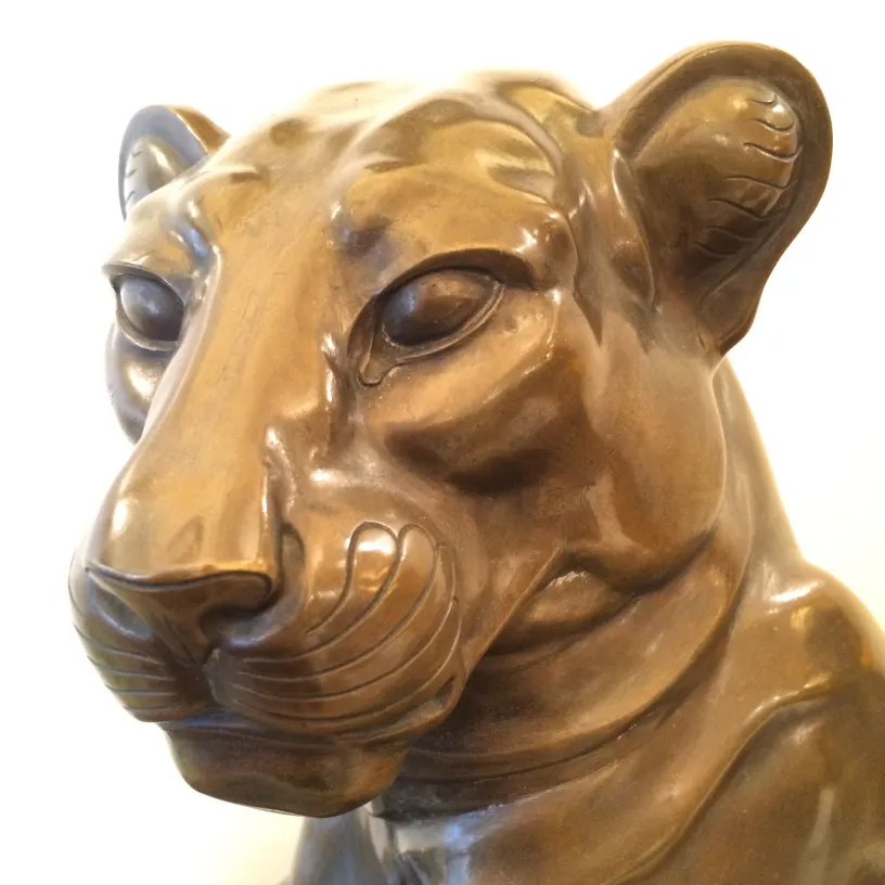 Scultura antica a forma di testa di leone, colore bronzo, dettagli realistici.