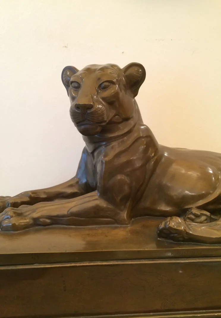 Scultura antica di una leonessa in posizione sdraiata, realistica.