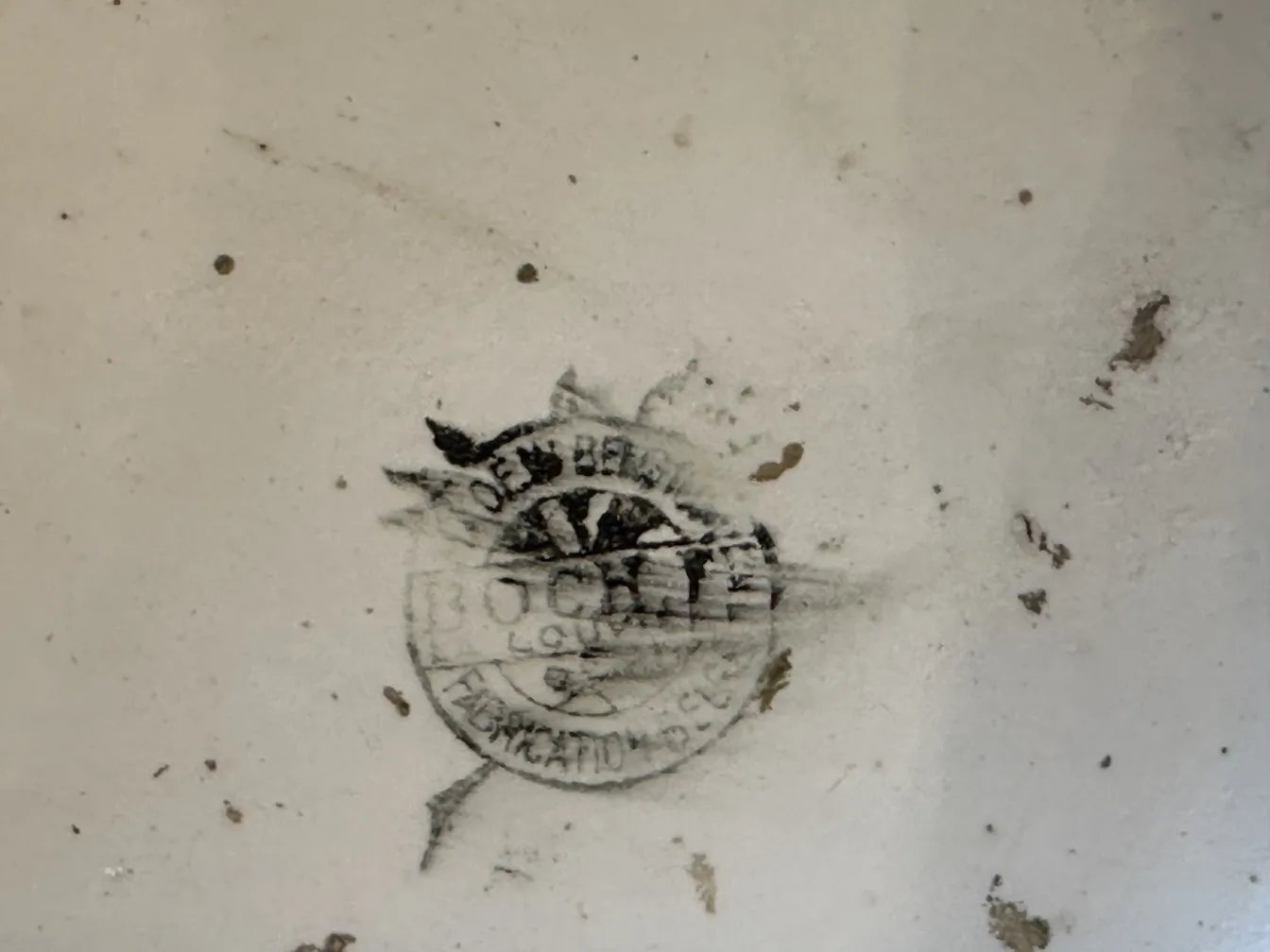 Sichtbarer Stempel von Boch frères auf antiker Keramik vor hellem Hintergrund, mit subtilen dekorativen Details und Flecken.
